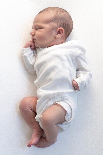 Photo sleeping newborn baby in a wrap on white blanket beautiful portrait of little child girl days one