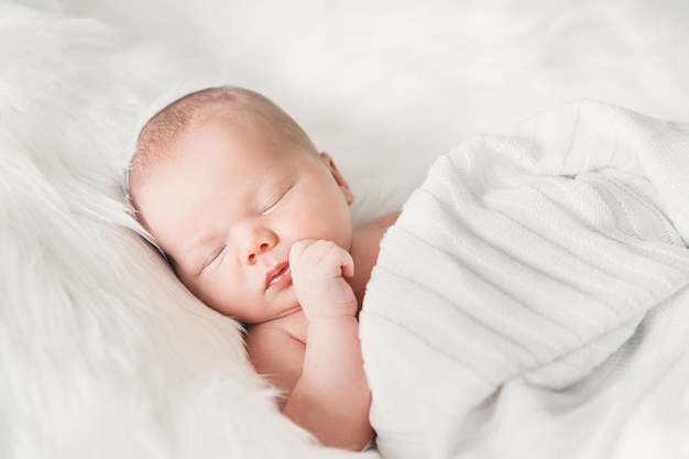 Sleeping newborn baby in wrap on white blanket Beautiful portrait of little child girl one week old