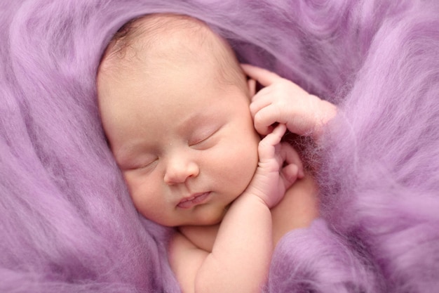 Sleeping newborn girl on a pink wool background closeup