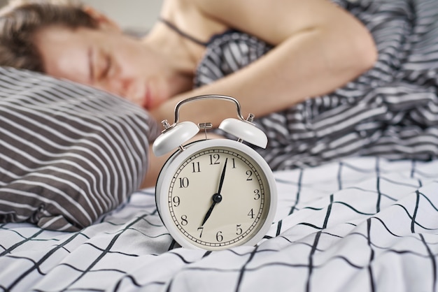 Sleeping woman in bedroom and vintage alarm clock. Wake up and morning concept