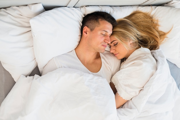Photo sleeping young couple under blanket on bed