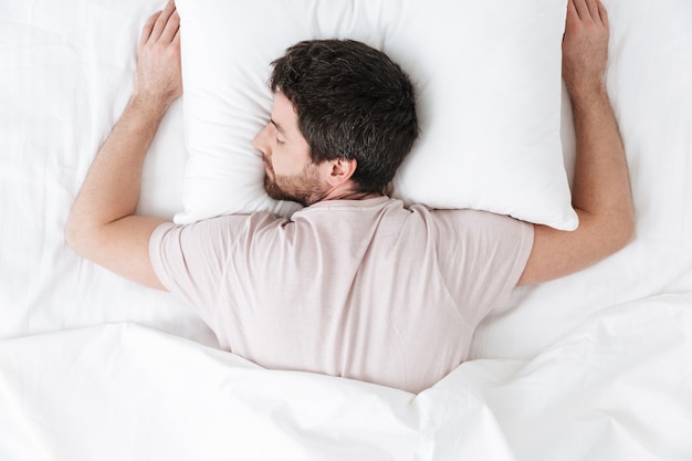 sleeping young man in the morning under blanket in bed lies