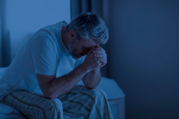 Sleepless depressed middle aged man sitting on bed at home