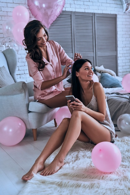 Sleepover beauty treatment. Two attractive young women in pajamas smiling while sitting in the bedroom with balloons all over the place