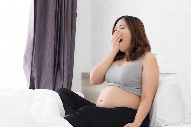 Sleepy asian pregnant woman yawning in bed at home