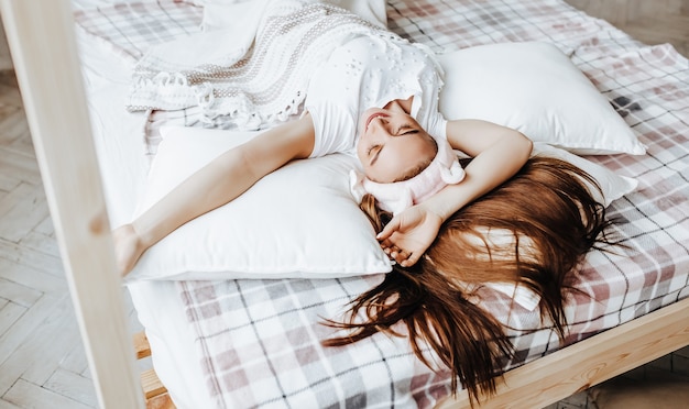 Photo a sleepy brunette girl lies in bed with a blindfold waking up in the morning