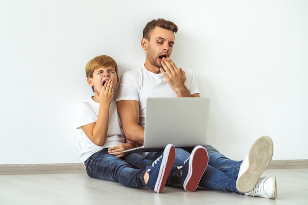 The sleepy father and a son with a laptop sitting on the floor