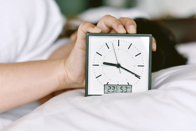 Sleepy girl's hand showing alarm clock