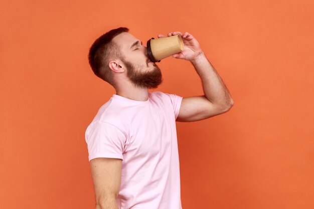 Sleepy man standing drinking coffee from disposable mug need energy in morning