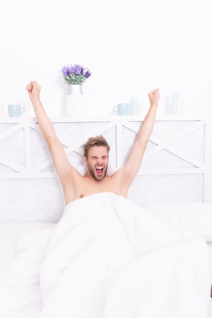 Sleepy man stretching on bed in white bedroom