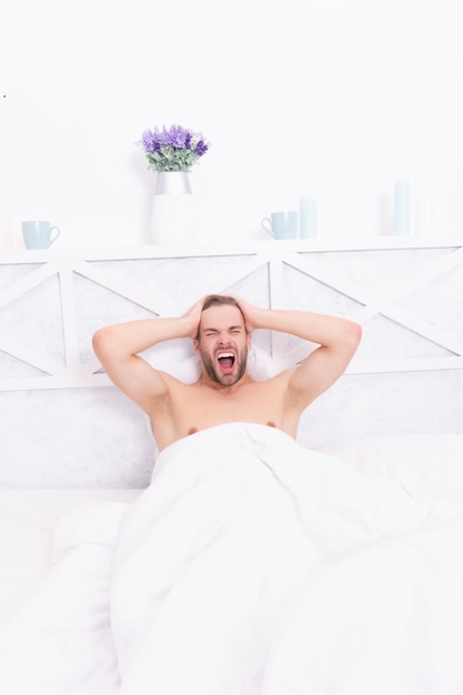 Sleepy man yawning on bed in white bedroom