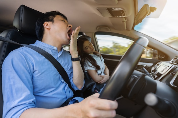 Sleepy man yawning while driving a car and his wife is sleeping