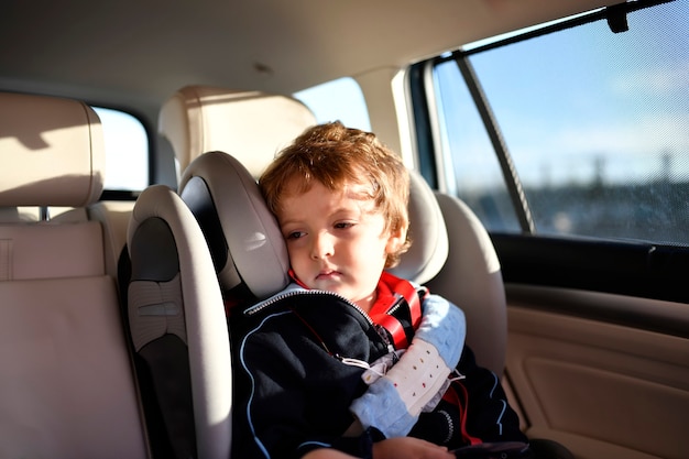 Sleepy three year old boy sitting in car safety seat going to school in the morning