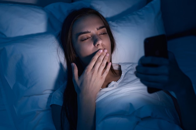 夜にスマートフォンを閲覧する眠そうな女性