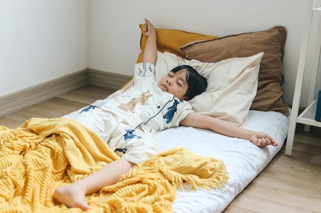 写真 ベッドで目覚めるのに手を伸ばす眠い若い少年