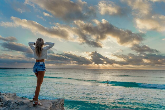 Slender blonde woman admires the sunrise at sea