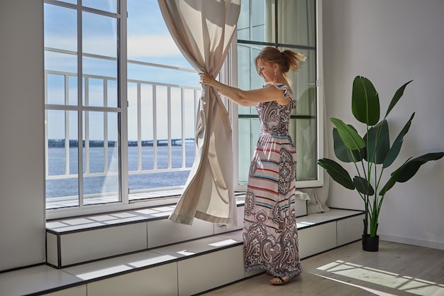 Photo slender caucasian woman pulls curtains in room