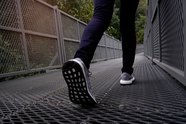 Slender female legs in blue jeans and grey sneakers walking along forest trail.