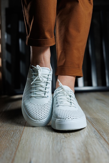 Скромные женские ноги в брюках крупный план в белых спортивных туфлях Женская кожаная обувь