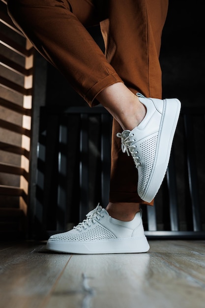 Slender female legs in pants closeup in white casual sneakers Women's leather shoes