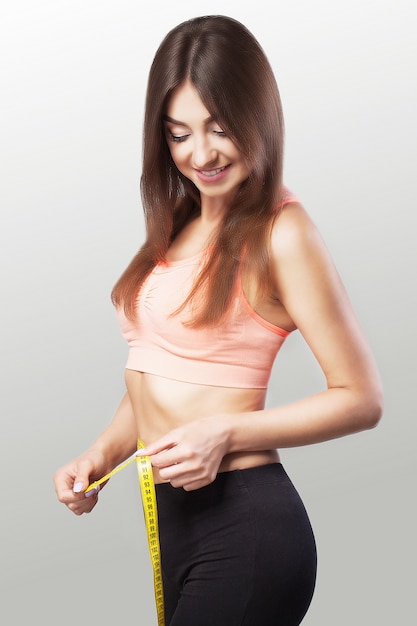 Slender girl. Hands to measure the waist tape. Fit and healthy woman on a gray background.