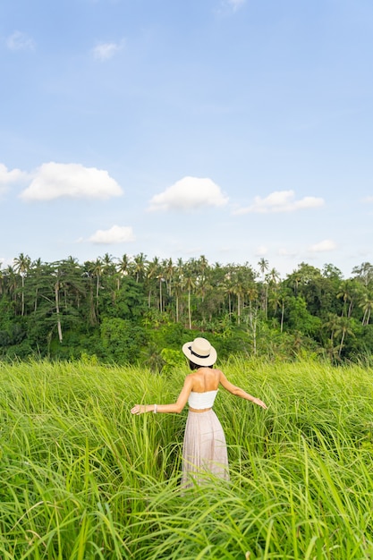 모자를 쓴 날씬한 소녀가 열대 국가로 여행하는 동안 쌀 농장을 걷고 있다