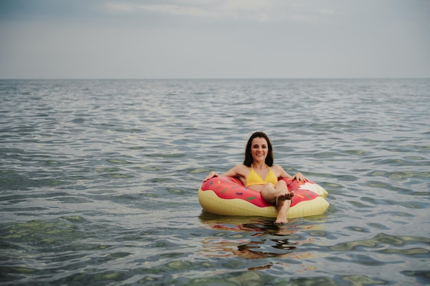 ほっそりした女の子は夏に海の膨脹可能な円で泳ぐ