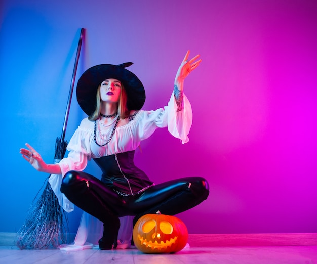 The slender girl in a witch costume for Halloween with a broom and a pumpkin