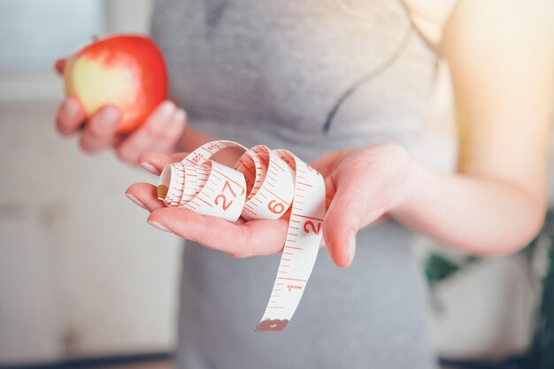 Slender girl with apple in her hand offers measuring tape with inches slimming concept