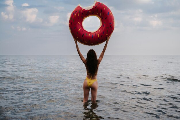 Slender girl with a sexy booty in a swimsuit holds an inflatable circle in her hands in the summer at the sea