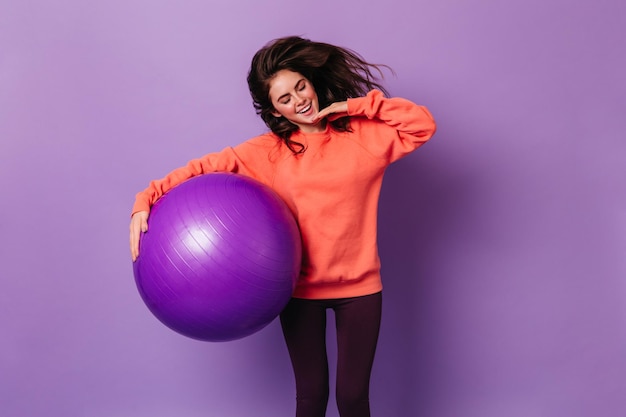 Slender lady holds huge fitball Woman in sport outfit smiling on isolated background