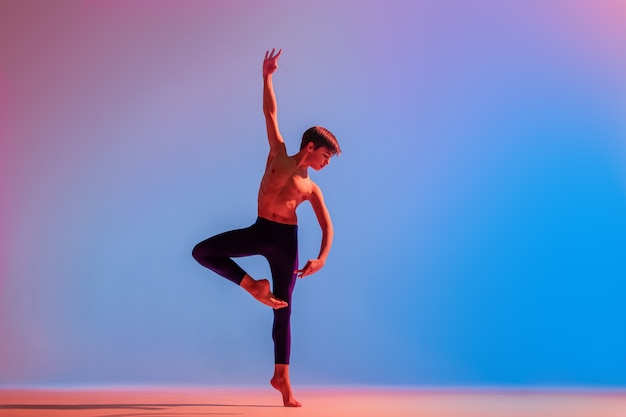 Slender teenage ballet boy dancer dances barefoot under a colored light.