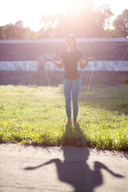 Slender woman athlete in sport apparel doing workout with jump rope at the sunset