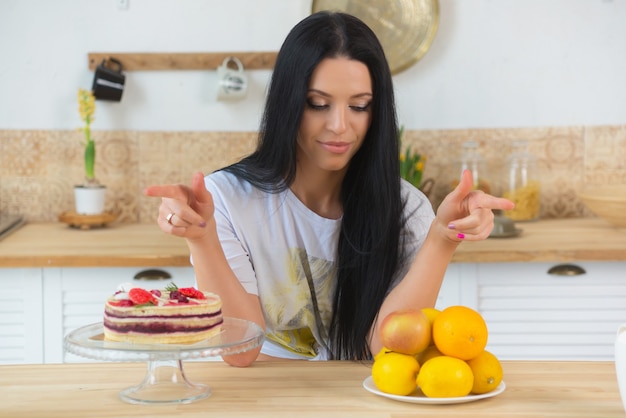 slender woman explains the benefits of proper nutrition holds fruit and cake in her hands compares unhealthy and healthy food