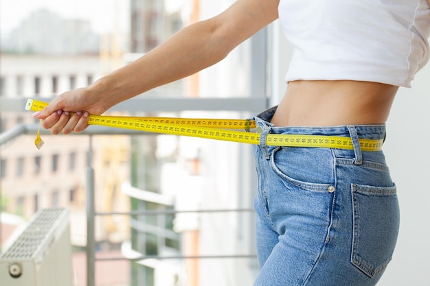 Slender woman in jeans and a white Tshirt measures her waist