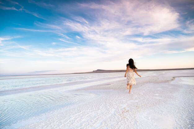 Una donna snella corre lungo la riva del mare in un vestito.