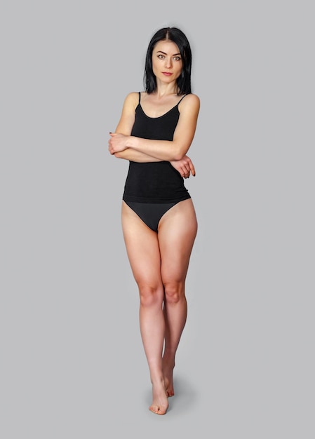 Slender woman standing in a black bodysuit on a gray background