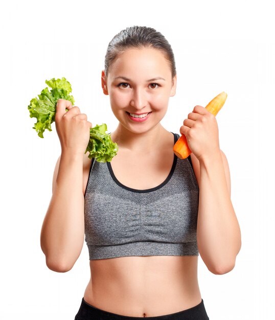 Slender woman with a beautiful figure holds vegetables in her hands - carrots and lettuce