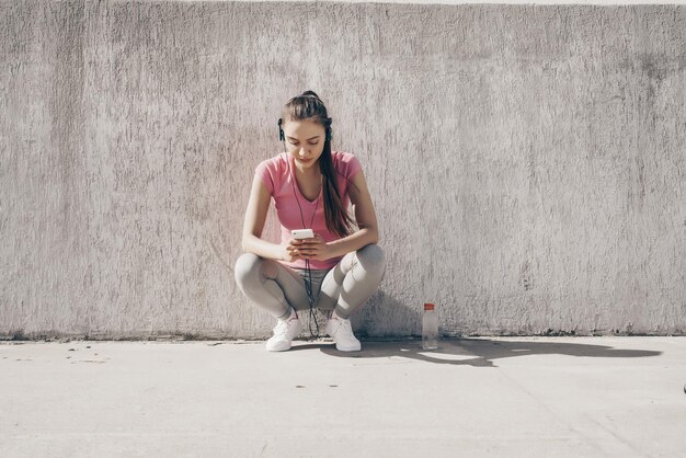 Slender young girl in a pink Tshirt listening to music on headphones and resting after jogging