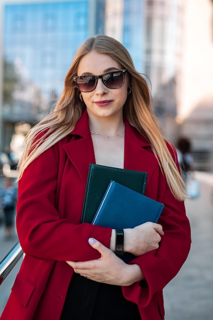 Slender young lady in a classic jacket with chic hair is smiling in the middle of the city