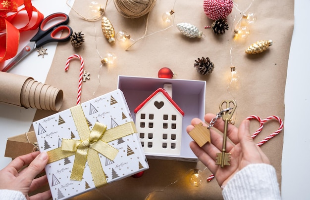 Sleutel tot huis met sleutelhanger aan knus huis in geschenkdoos met kerstdecorverpakking Pak cadeau voor Nieuwjaar Kerst Bouwproject verhuizing naar nieuw huis hypotheek huur aankoop onroerend goed