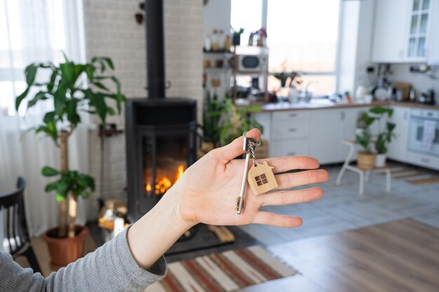 Sleutel tot huis met sleutelhanger tegen achtergrond van open haardkachel met vuur en brandhout Gezellige huishaard Bouwontwerpproject verhuizen naar nieuw huis hypotheek huren en onroerend goed kopen