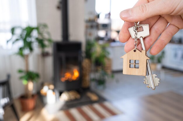 Sleutel tot huis met sleutelhanger tegen achtergrond van open haardkachel met vuur en brandhout Gezellige huishaard Bouwontwerpproject verhuizen naar nieuw huis hypotheek huren en onroerend goed kopen