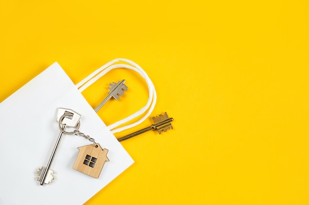 Sleutelring van houten huis met sleutel op een gele muur in een witte papieren zak.