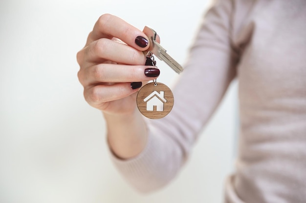 Sleutels van onroerend goedconcept met een sleutelhanger in de vorm van een huis in de hand van een vrouw