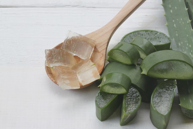 Fetta di aloe vera è in un cucchiaio di legno posto su un legno bianco.