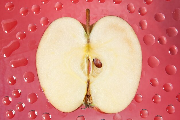 Photo slice an apple on a red wallin the drops.