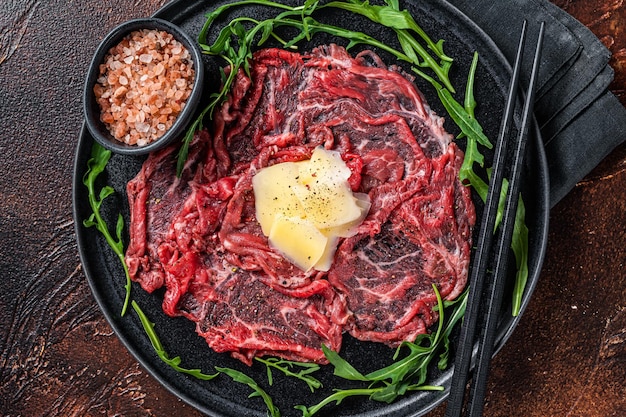 Slice Of beef Carpaccio, arugula and Parmesan. Dark background. Top view.