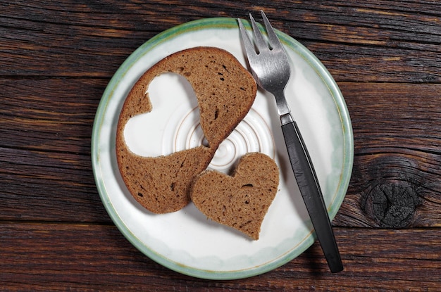 Slice black bread with cut in shape of heart and fork on plate top view