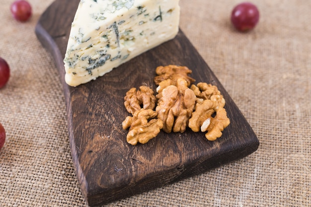 Photo slice of blue cheese with nuts and grapes on a rustic wall.